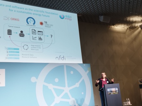 Astrid Nieße talking at the conference. On the left side the presentation screen can be seen. She is standing behind a podest